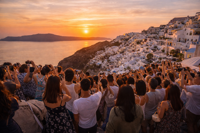 Crowded Santorini sunset viewpoint with tourists gathered closely together overlooking the caldera, illustrating peak season congestion