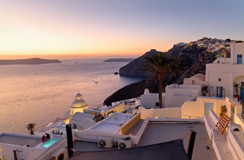 Romantic sunset view of Oia Santorini with white cliff side buildings overlooking the Aegean Sea.