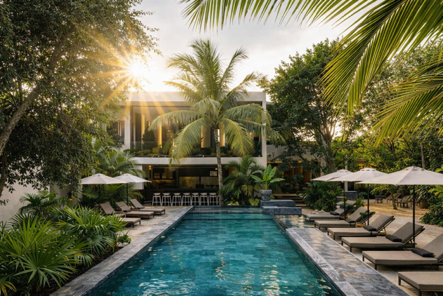 Modern luxury villa in Tulum surrounded by palm trees with large infinity pool and tropical outdoor lounge area at sunset